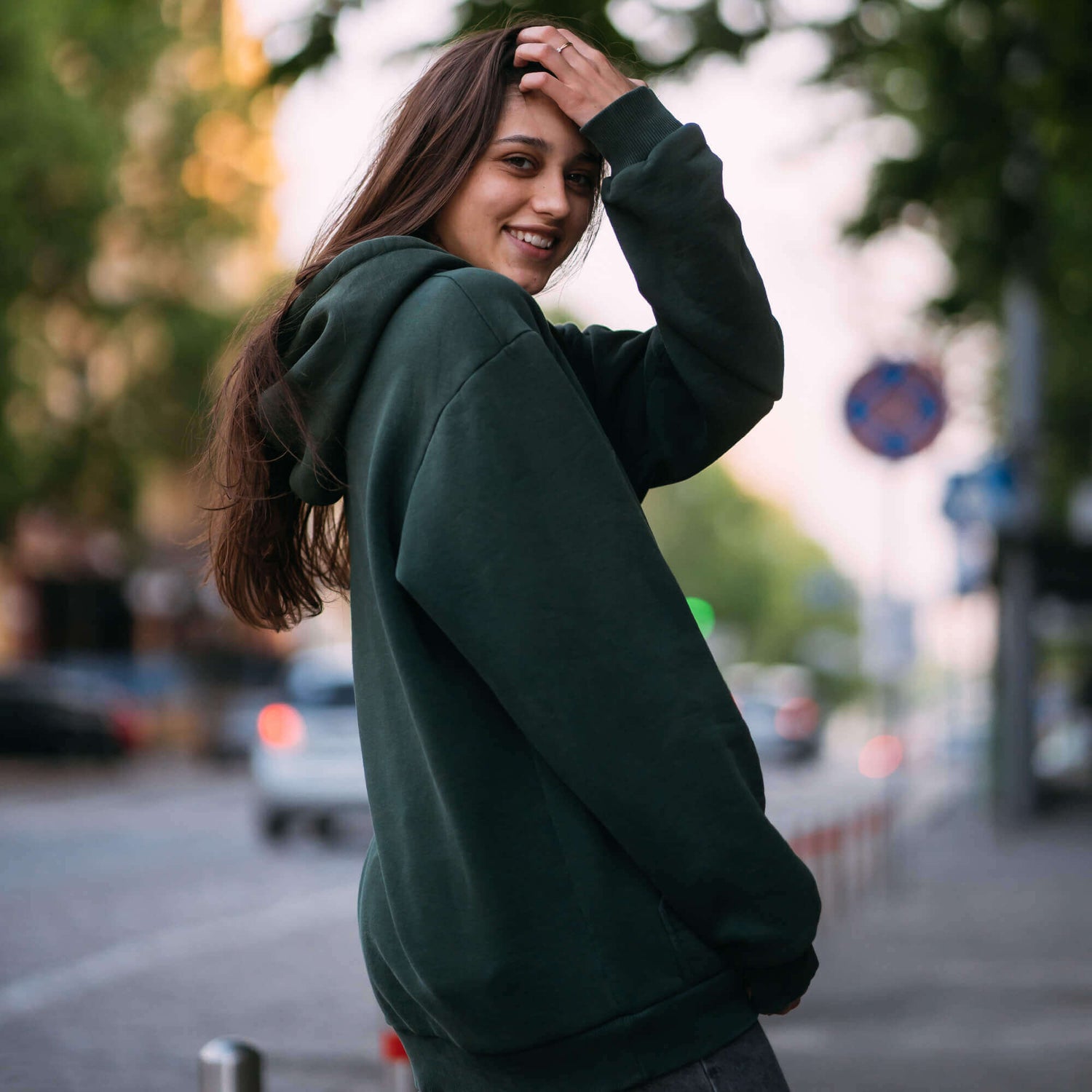 a woman in a green hoodie standing on a sidewalk