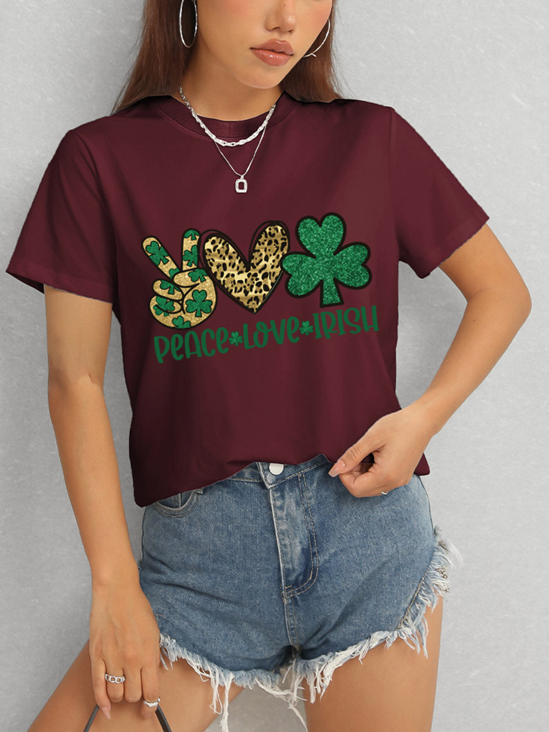 Model in burgundy Peace Love Irish T-Shirt and denim shorts