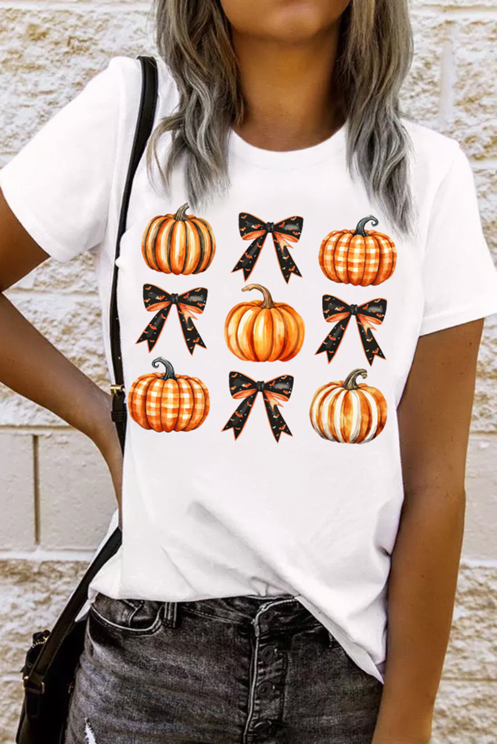 White T-shirt with pumpkin and bow design, worn by model.