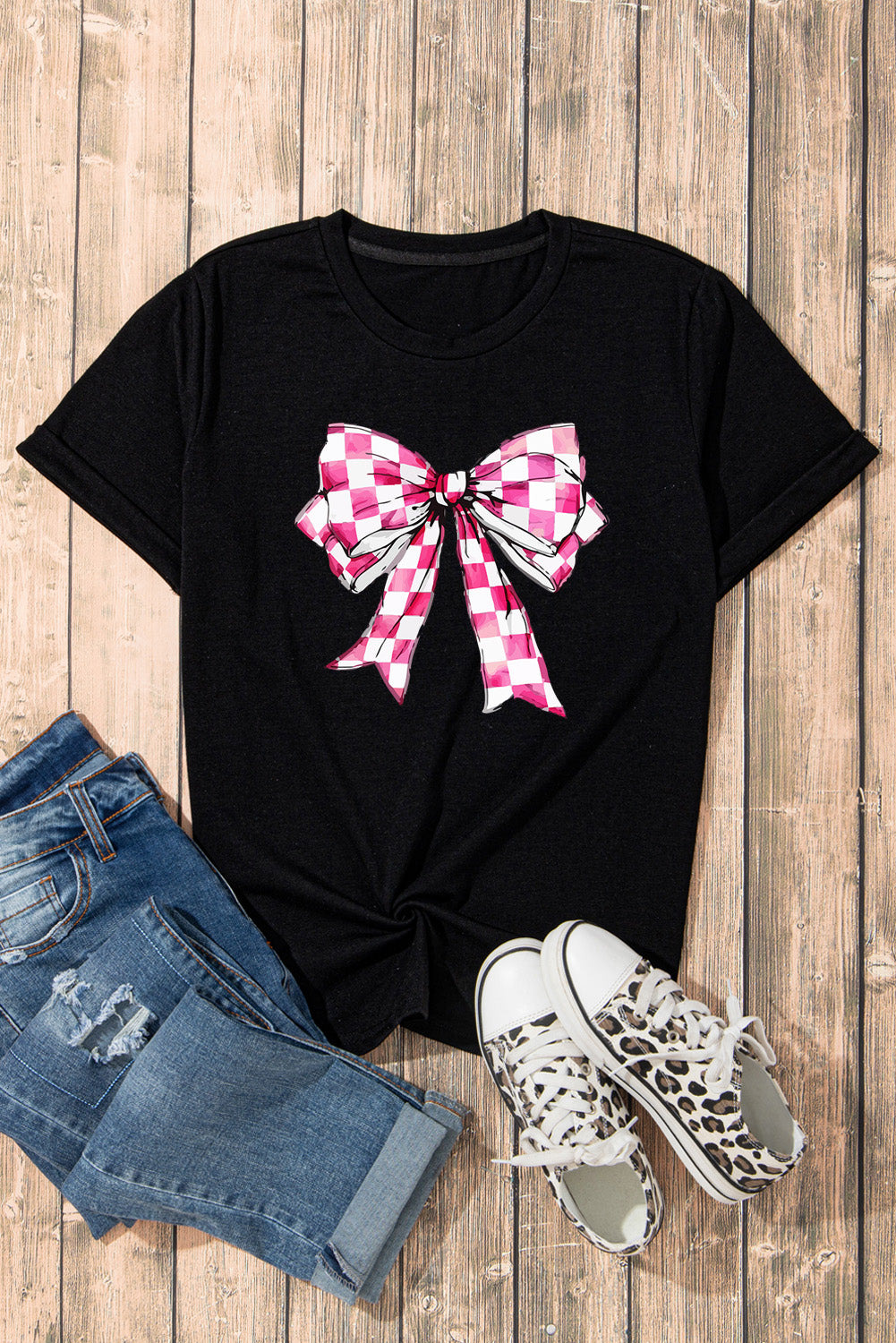Flat lay of black T-shirt with pink bow, denim shorts, sneakers.