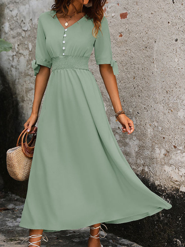 Model in green V-neck belted midi dress holding a straw bag.