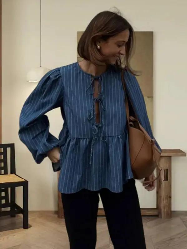 Woman in a blue striped lace-up top with a brown bag indoors
