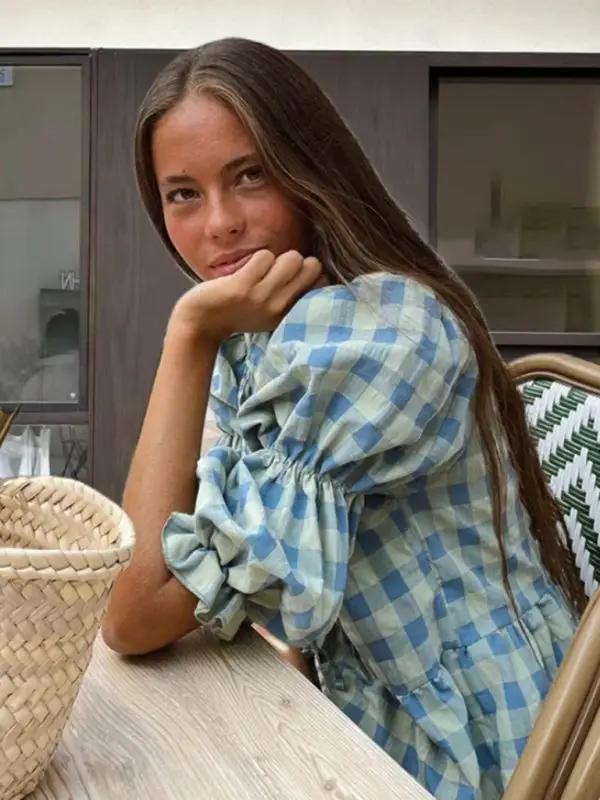 Blue checkered puff sleeve blouse with tie detail, seated woman