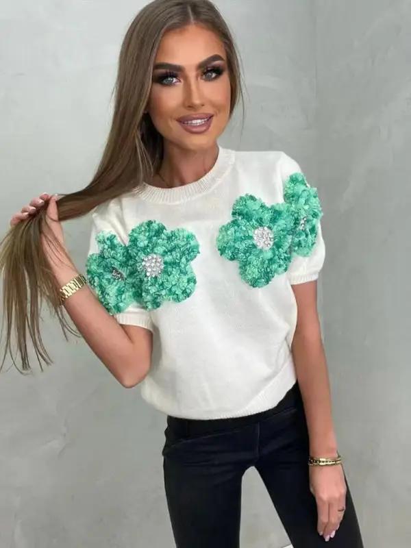 White sweater with green floral design, styled with black pants.