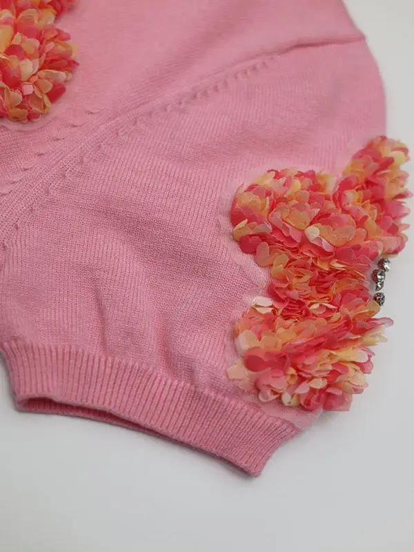 Pink sweater with floral accents, sleeve detail.