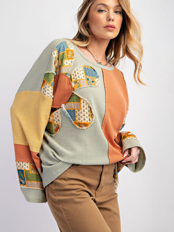 Green and orange contrast print waffle top with brown pants.