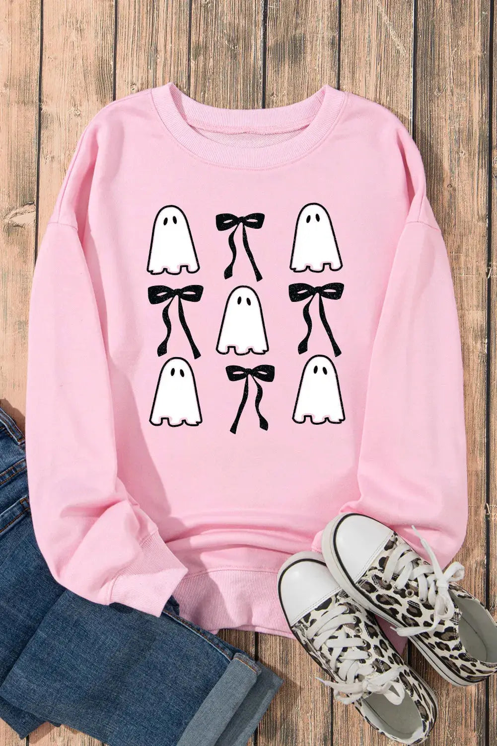 Ghost and bow design sweatshirt laid flat with jeans and sneakers.