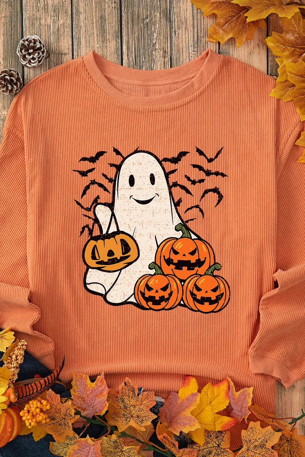 Flat lay of ghost and pumpkins sweatshirt with autumn leaves