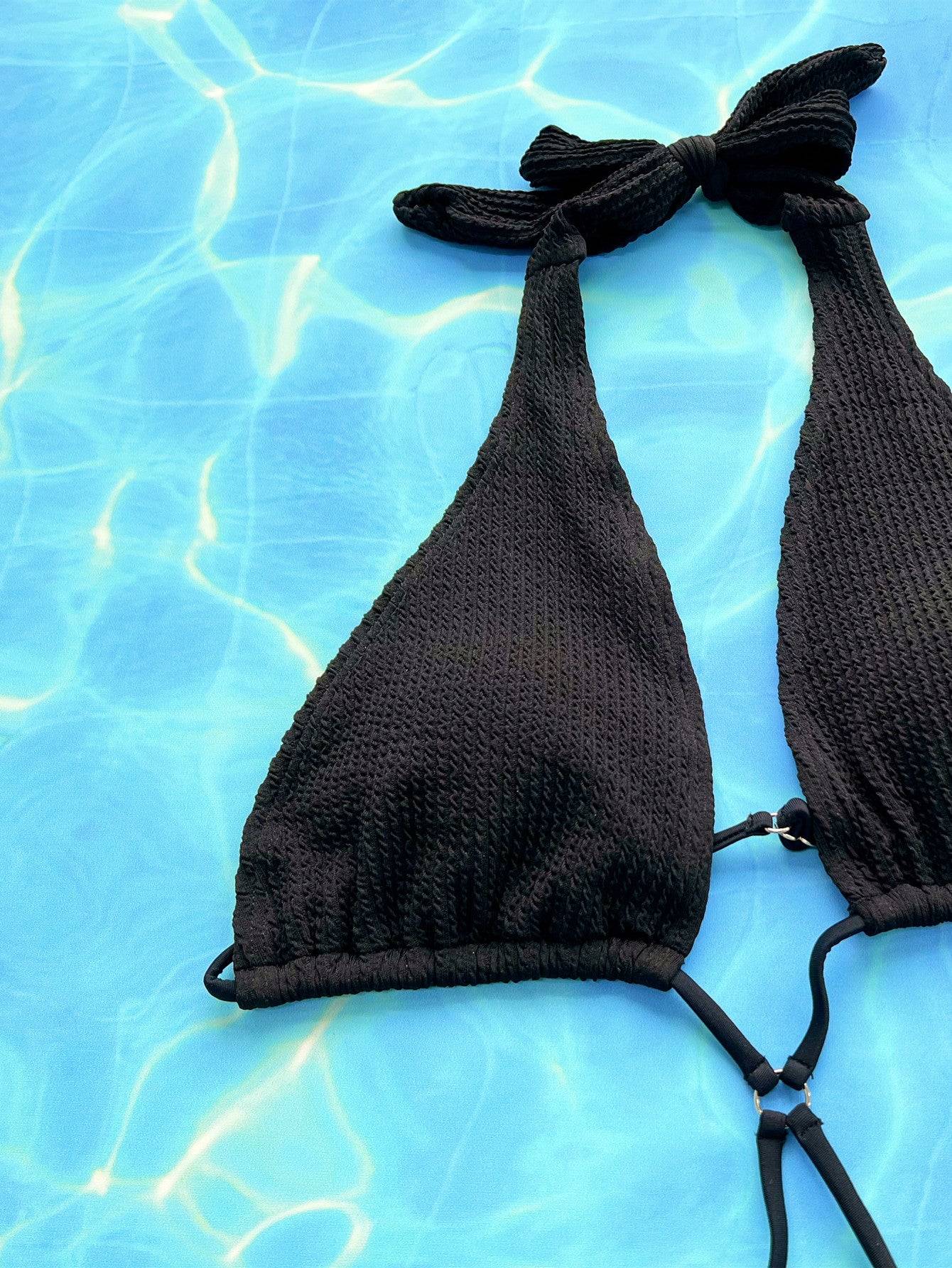 Close-up of black halter neck swimsuit top on blue background