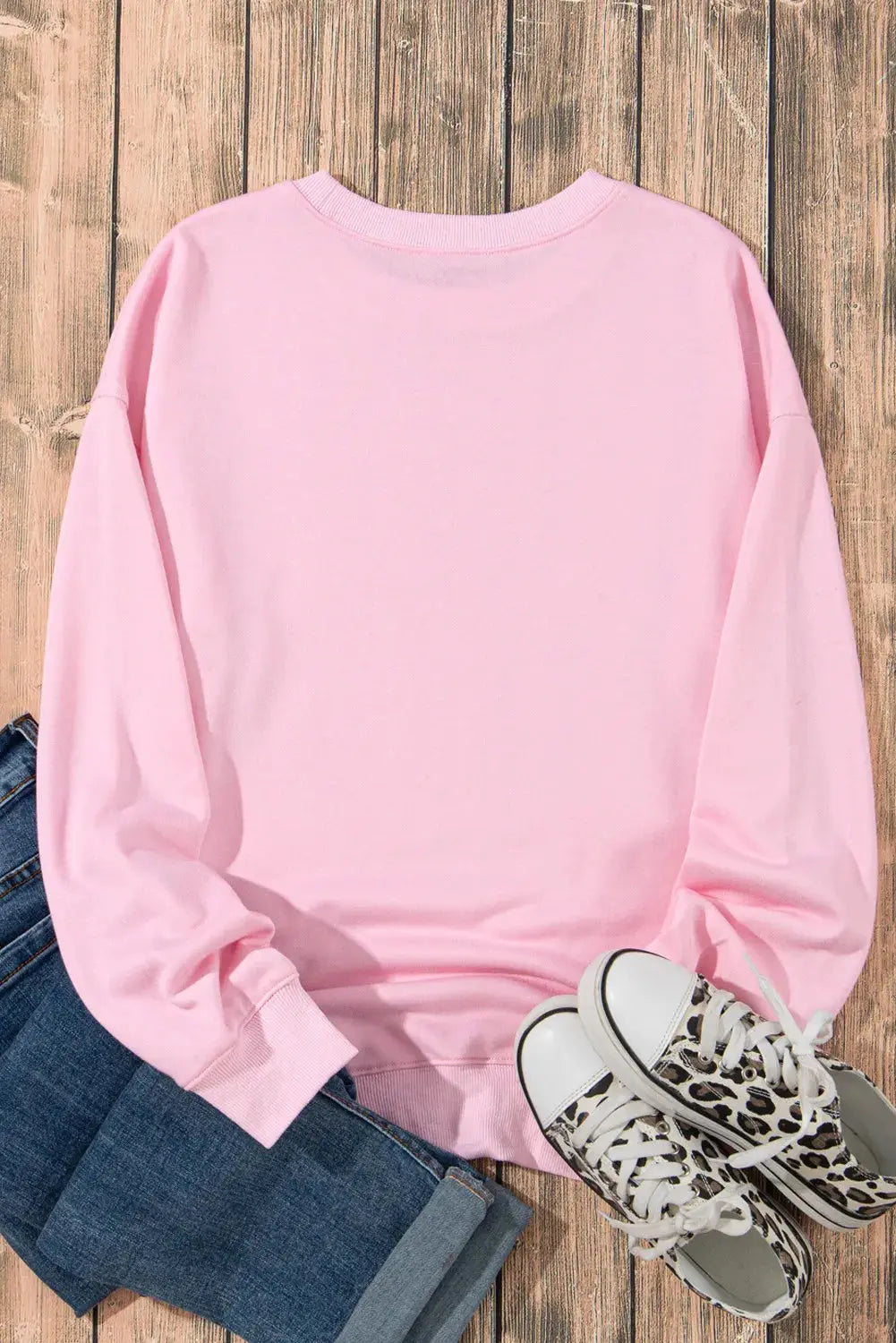 Back of pink sweatshirt displayed with jeans and sneakers.