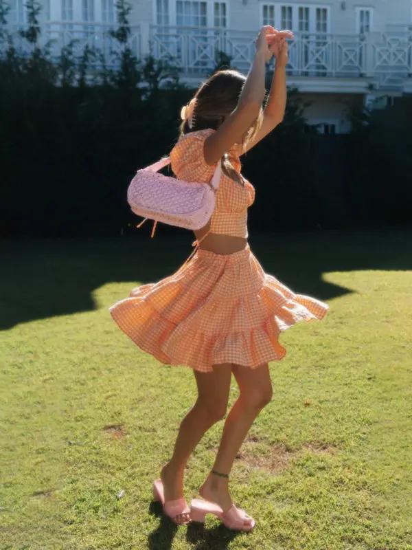 Woman twirling in orange plaid backless tie top and skirt