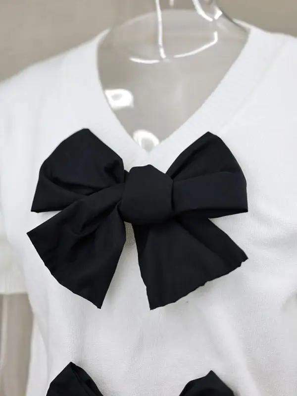 White V-neck sweater with black double bows, close-up view