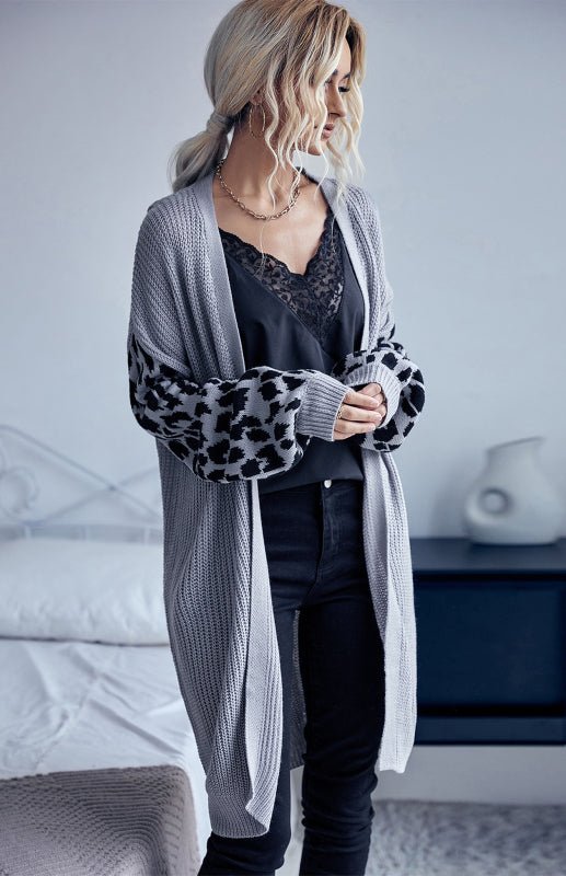 a woman standing in front of a bed wearing a cardigan
