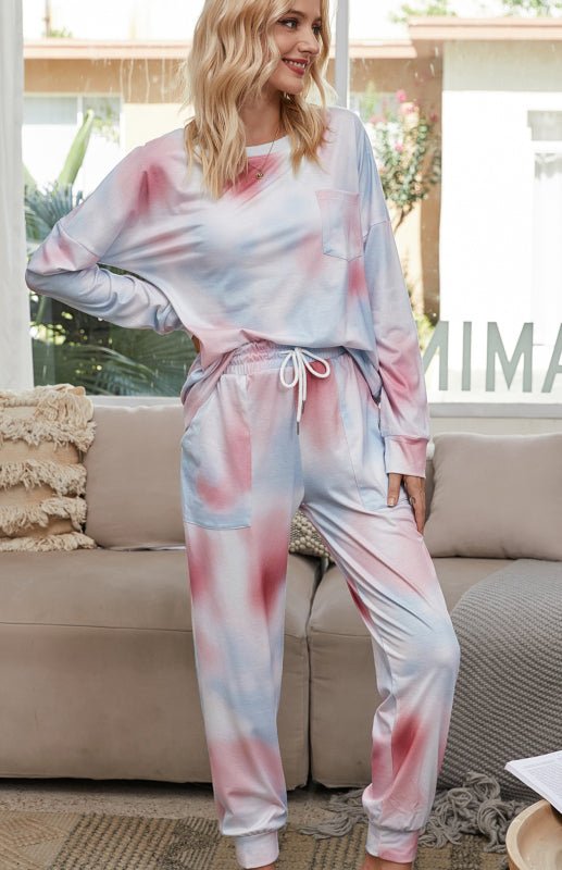 a woman standing in a living room wearing a pink and blue tie dye pajamas